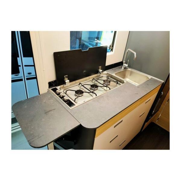 Cocina de la autocaravana Adria Coral XL 600 DP Axess con mesa, fregadero y fuegos con la tapa abierta